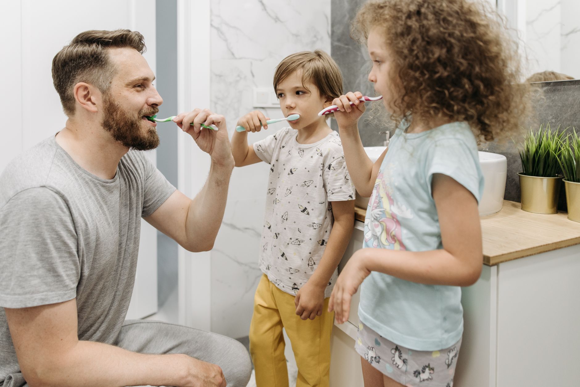 A father and his two children brushing their teeth in a brig מי מטפל בשיניים שלך - ד