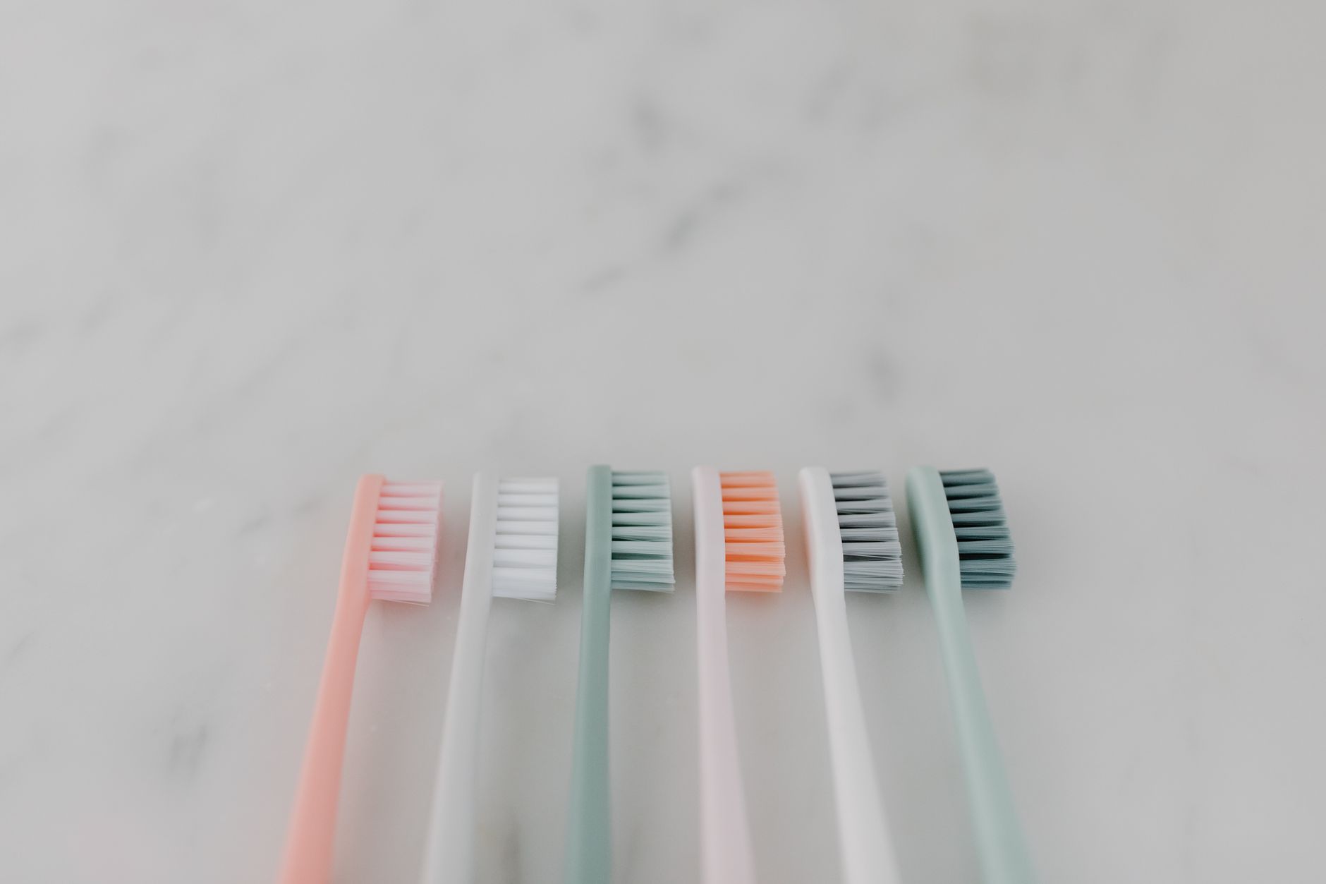 A row of colorful pastel toothbrushes aligned on a smooth ma כיצד מנקים שיניים - ד